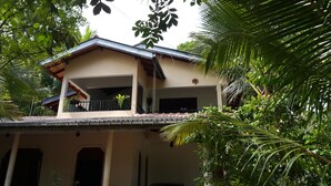 A two-story building with a balcony, surrounded by lush greenery.