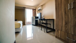 A hotel room with a bed, a desk with a computer, a wardrobe, and an air conditioning unit. - Sea Land View (Si Racha)