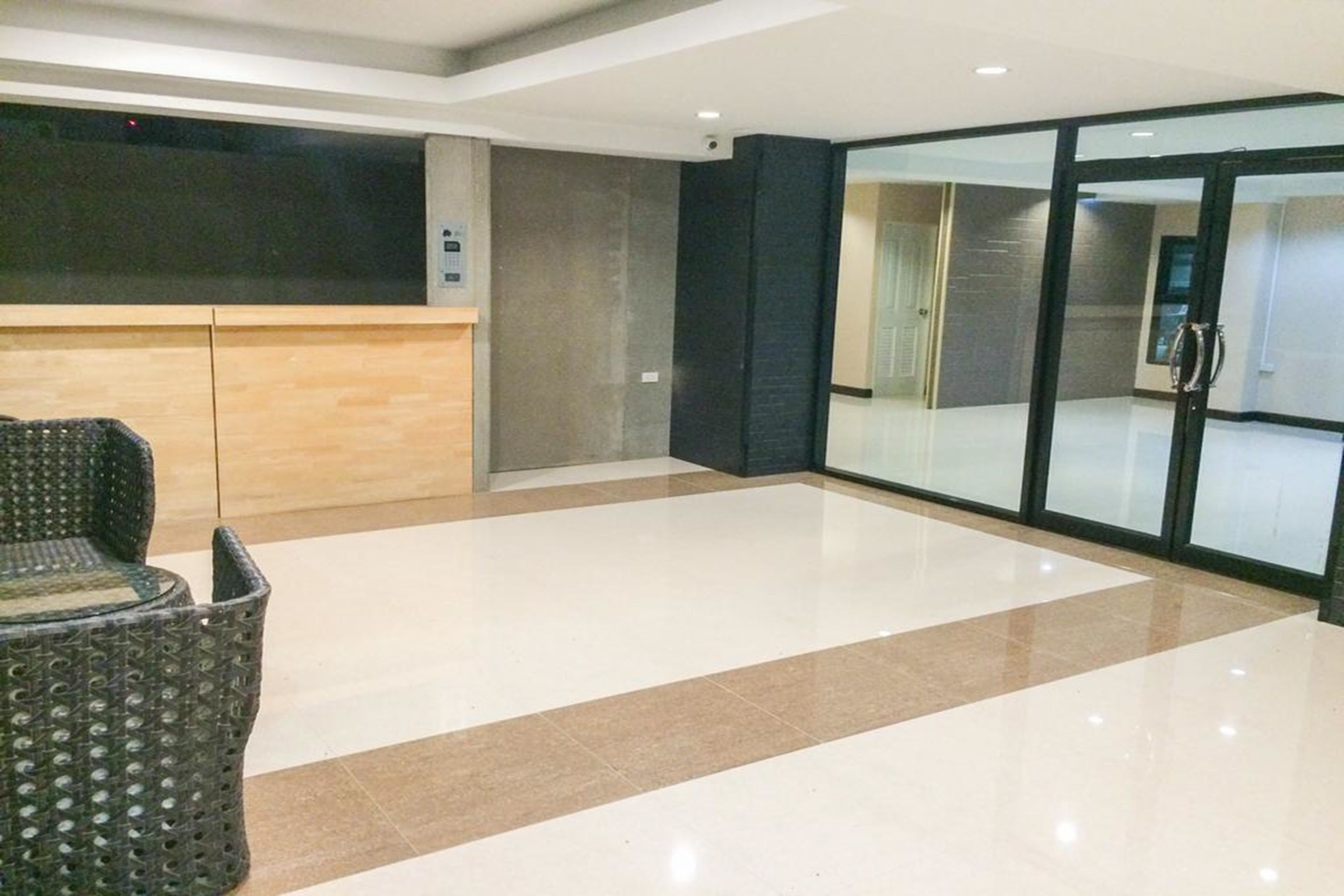 A spacious lobby with a reception desk, a seating area, and a glass door leading to another room.