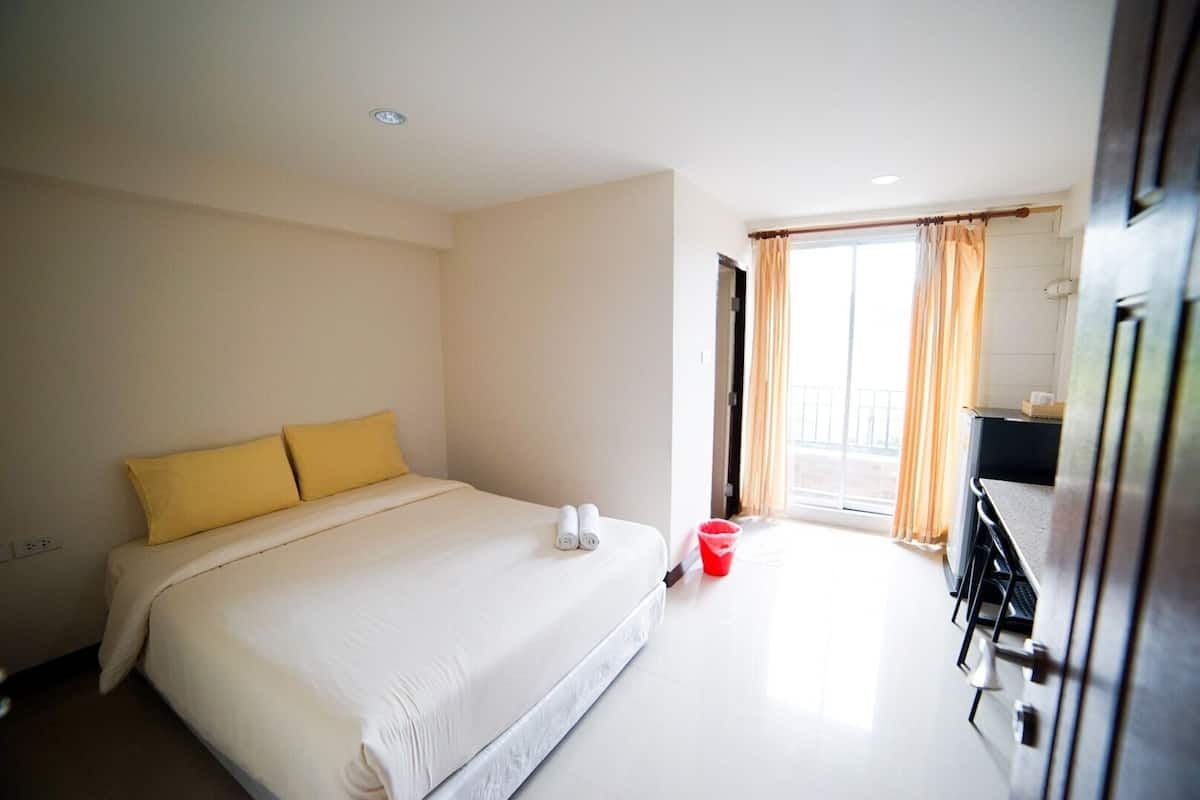 Une chambre d’hôtel avec un grand lit, un petit bureau et une fenêtre avec des rideaux.