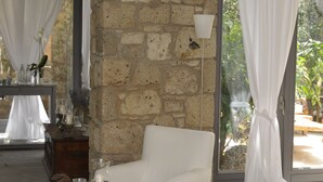Una habitación con un sofá blanco, una pequeña mesa de madera con libros y una vela, y una pared de piedra.