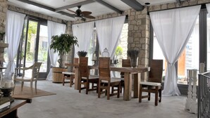 Un patio techado con pared de piedra, sillas de madera, una mesa y un ventilador de techo.