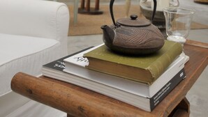 Una sala de estar acogedora con una chimenea de piedra, un sofá blanco y una mesa con libros y un hervidor de agua.