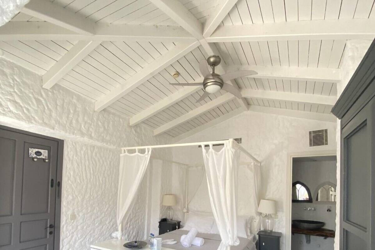 A bedroom with a four-poster bed, a ceiling fan, and a small bedside table with a lamp.