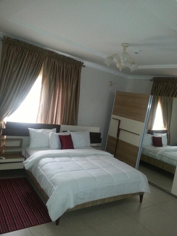 Quarto de hotel com uma cama grande, mesa de cabeceira, espelho e janela com cortinas.