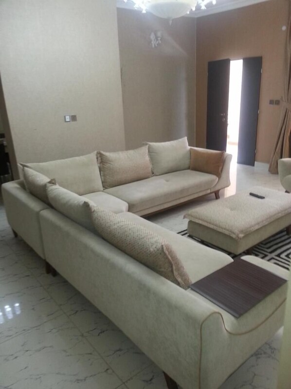 Una sala de estar con un sofá seccional color beige, un puf a juego y una mesita.