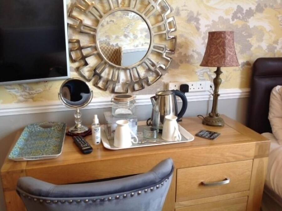 A wooden desk with a mirror, a kettle, a tray, and a remote control.