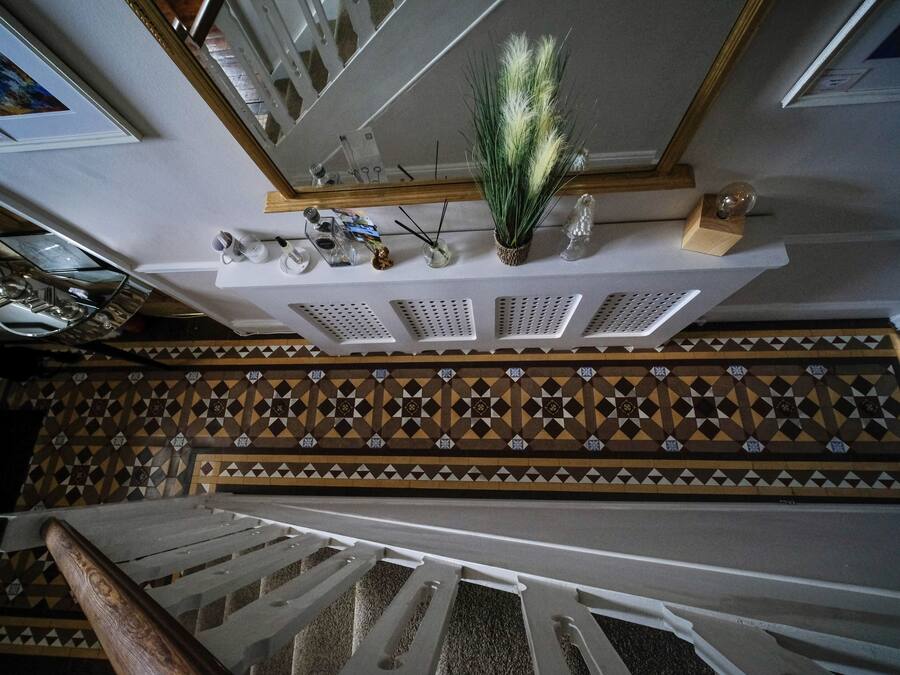 Una escalera con un muro de diseño, un techo con detalles decorativos y un pequeño estante con varios objetos.