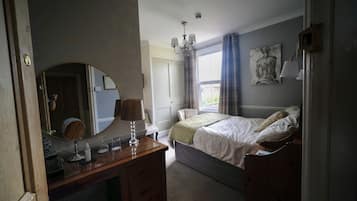 Un dormitorio con cama, cómoda, espejo, candelabro y ventana con cortinas.
