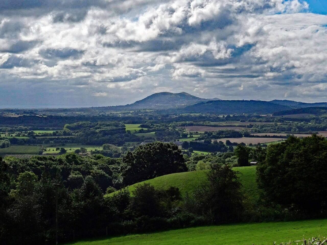 Una vista panorámica de un paisaje rural con colinas onduladas, una montaña a lo lejos y un cielo parcialmente nublado.