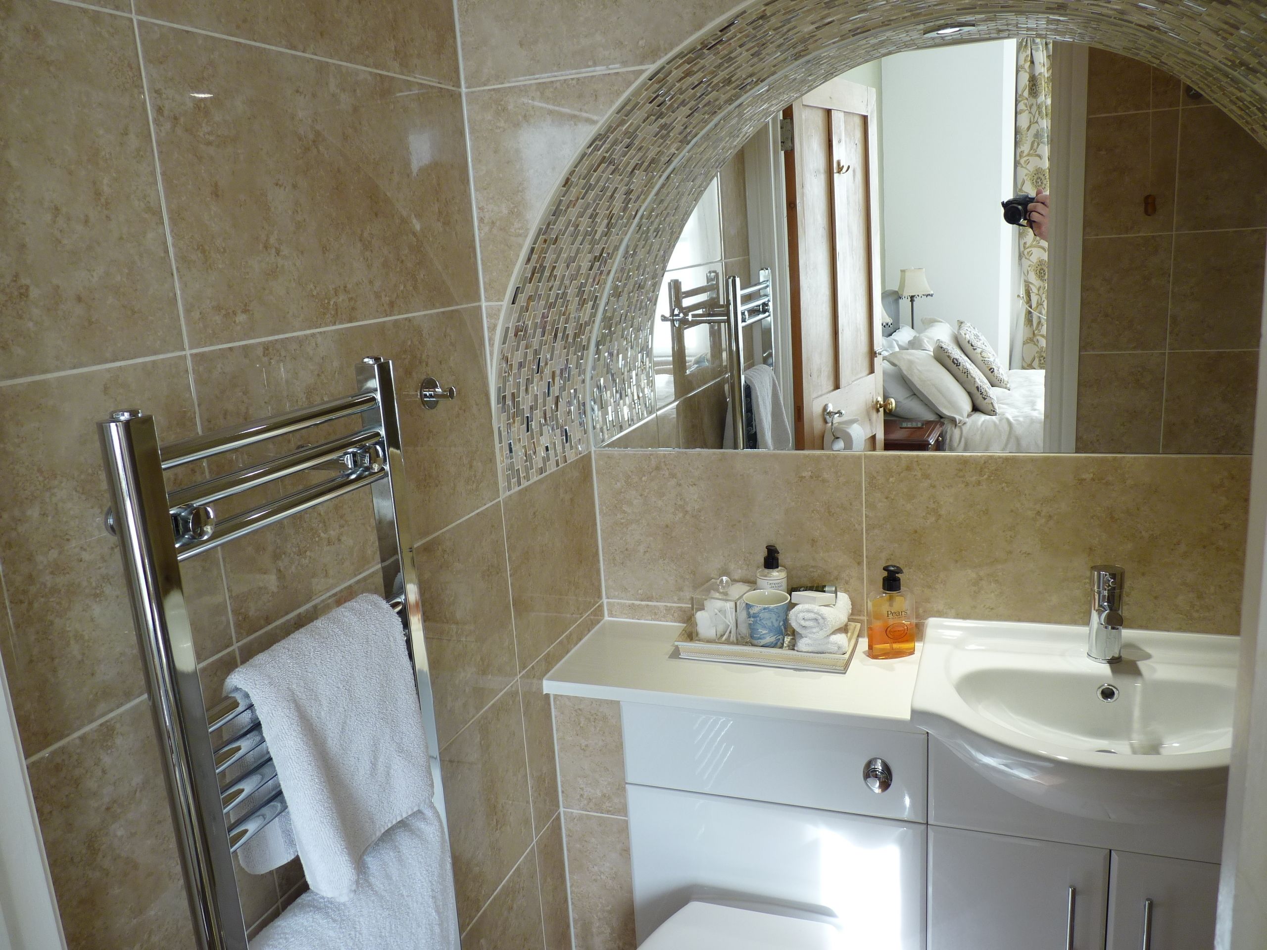 A bathroom with a tiled floor, a towel rack, a mirror, a sink, and toiletries.