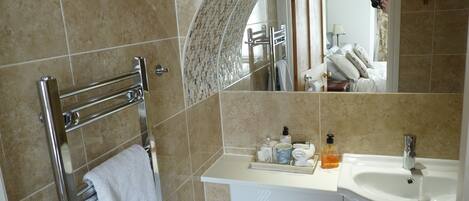 A bathroom with a tiled floor, a towel rack, a mirror, a sink, and toiletries.