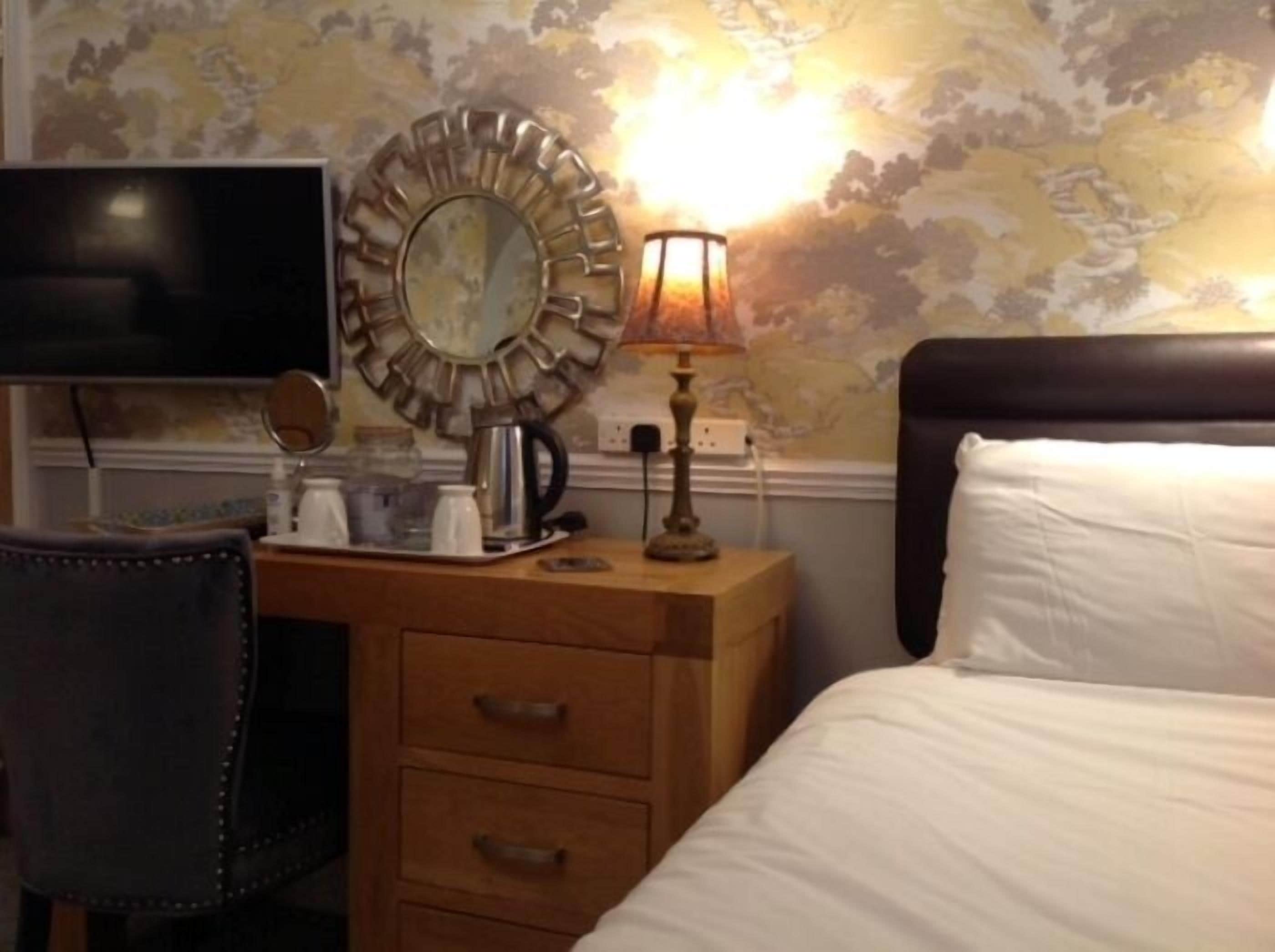 Une chambre d’hôtel comprenant un lit, un bureau avec une lampe, une télévision et une horloge murale décorative.