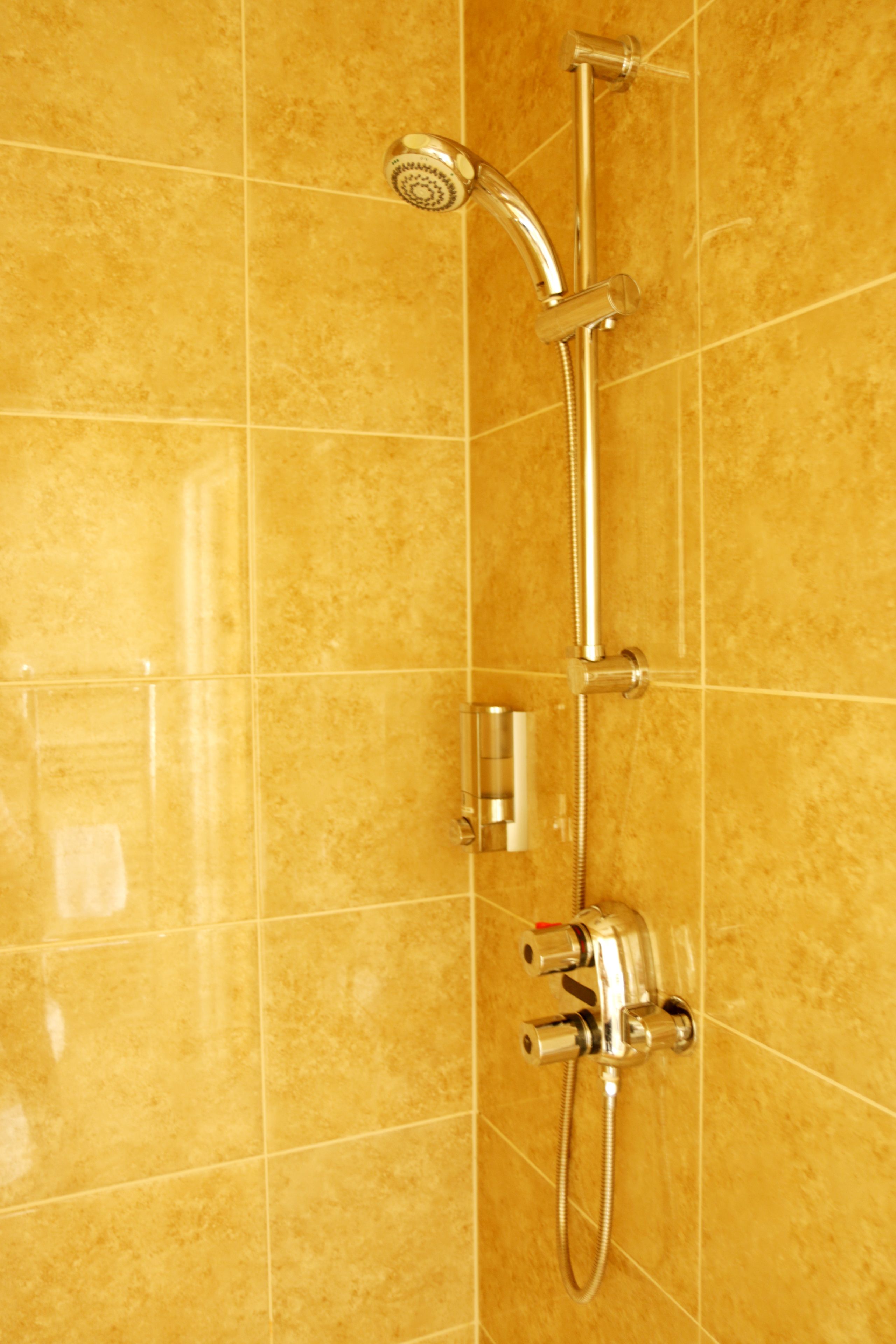 A bathroom with a shower system, including a handheld showerhead and a wall-mounted faucet.