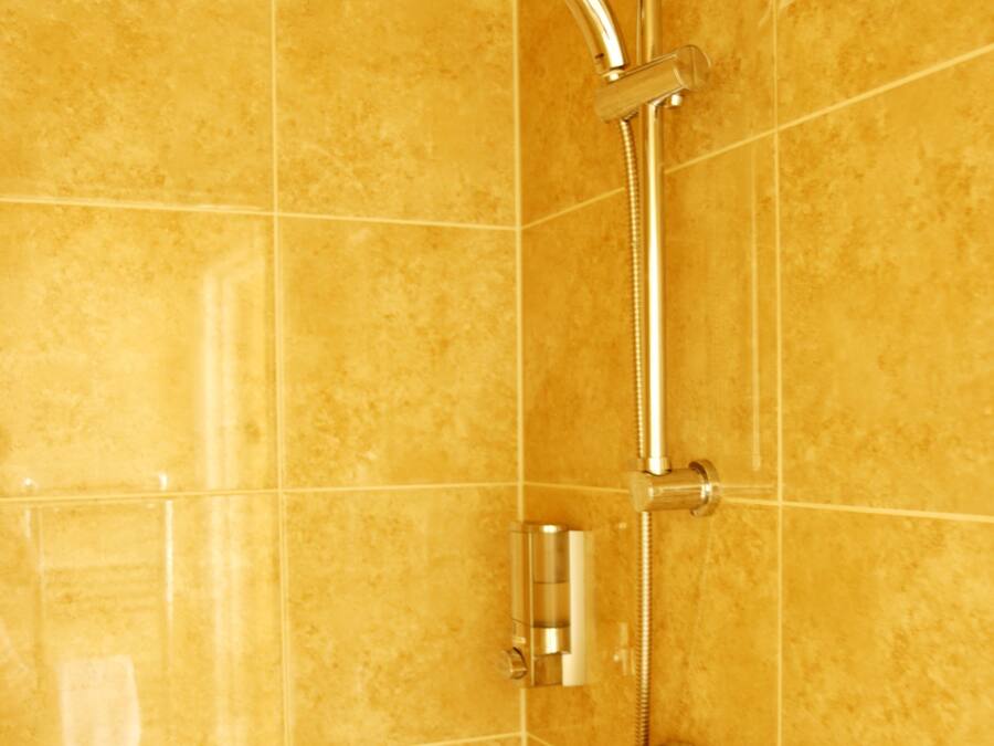 A bathroom with a shower system, including a handheld showerhead and a wall-mounted faucet.