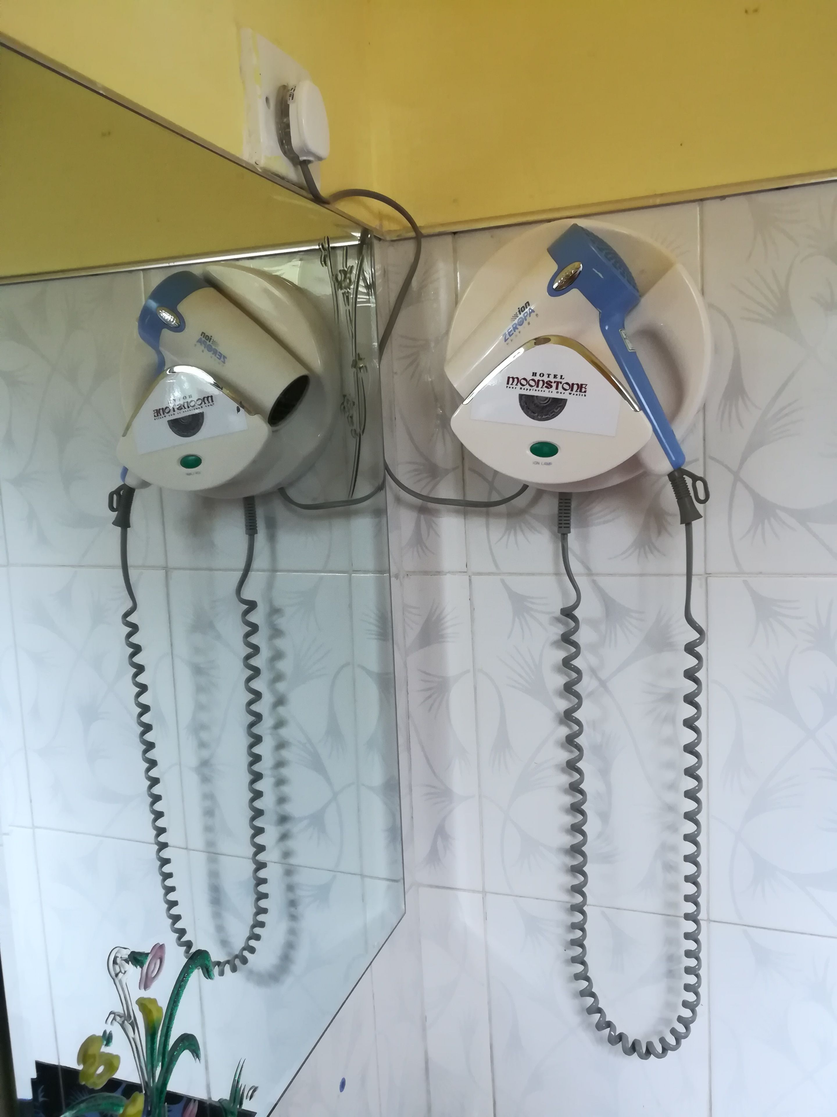 Een badkamer met twee aan de muur bevestigde haardroger, verbonden door opgerolde snoeren.