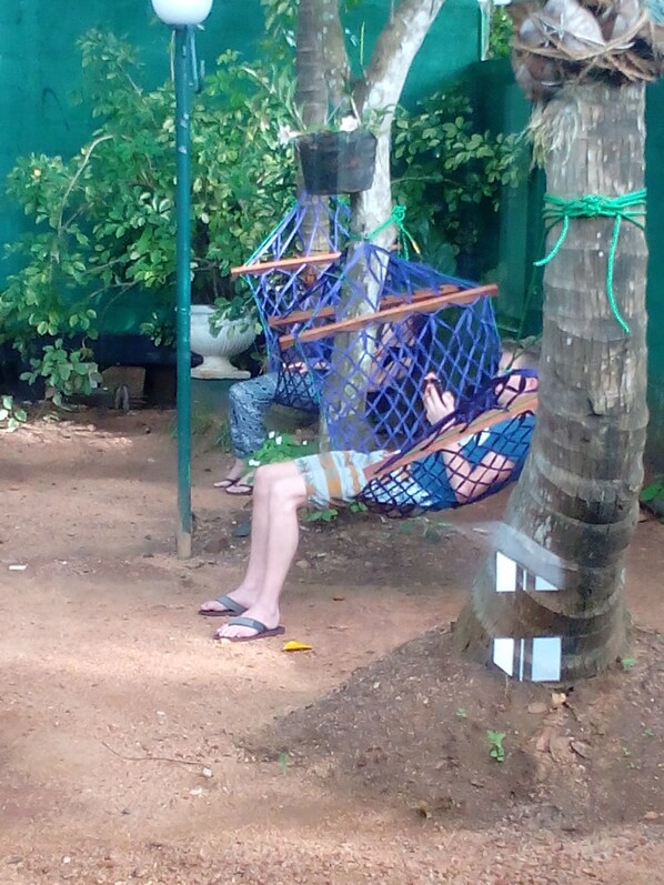 A person sitting on a hammock attached to a tree in an outdoor setting.