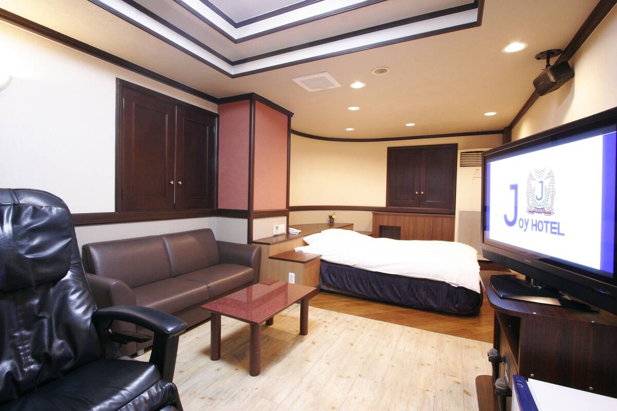 A hotel room with a bed, a desk, a television, a leather chair, and a sofa.