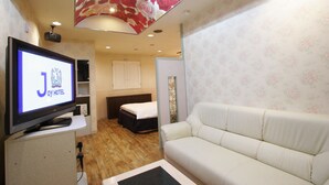 A hotel room with a television displaying 'J OY HOTEL', a white sofa, a bed, wooden flooring, floral wallpaper, and a ceiling with a floral design. - Hotel Joy -Adult Only (Komaki)