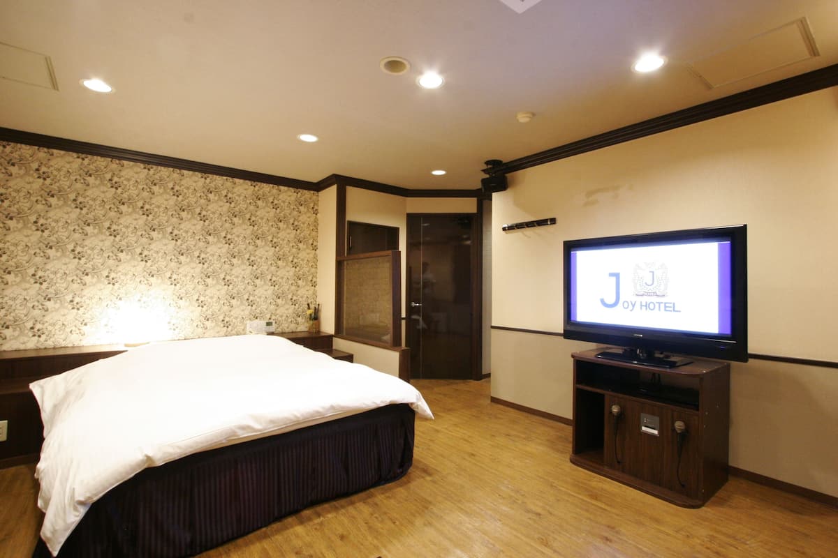 A hotel room with a bed, a television, and a wooden floor.