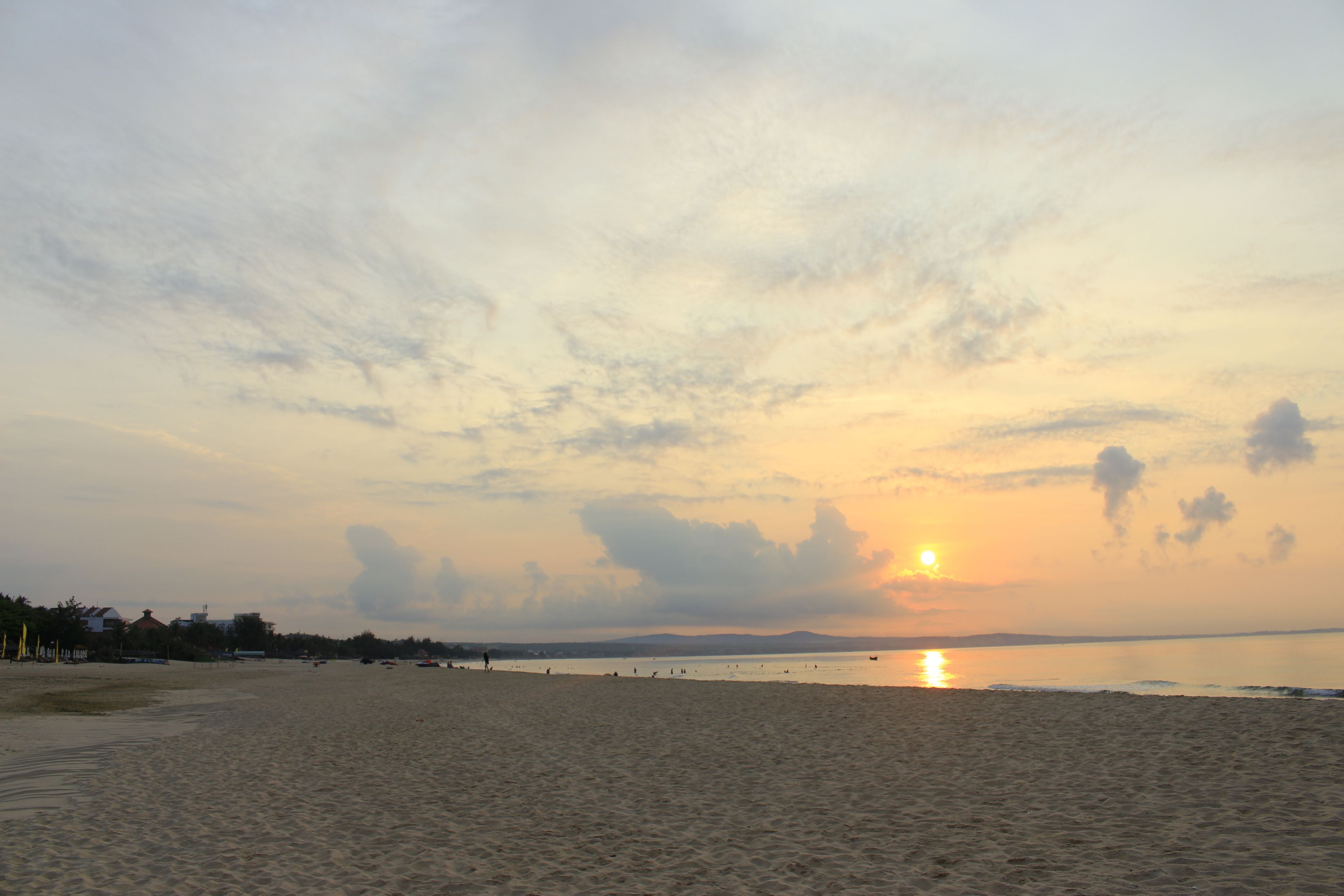 Een strand bij zonsondergang, met kalm water en bergen in de verte.