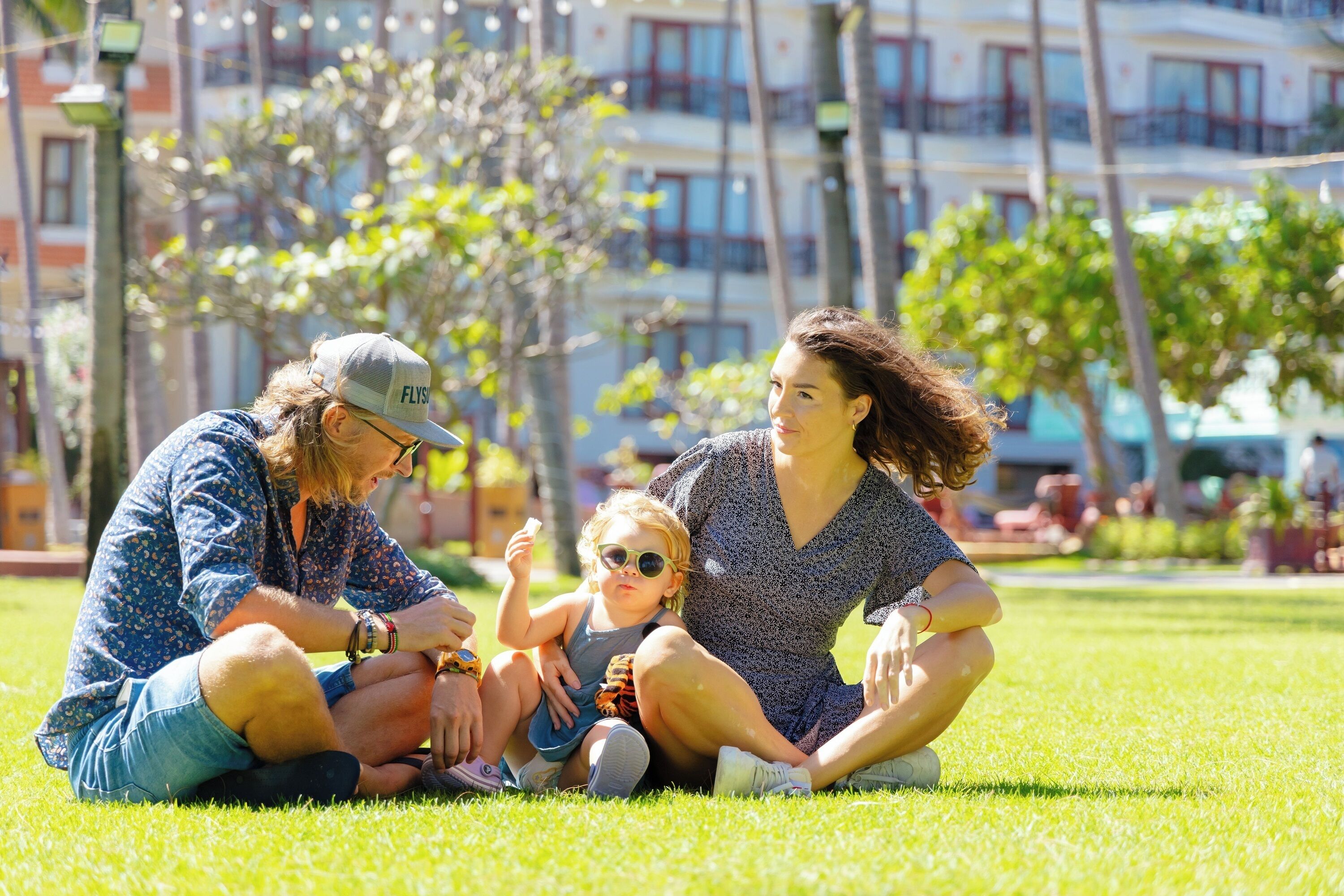 A family sitting on grass in a park with buildings in the background.