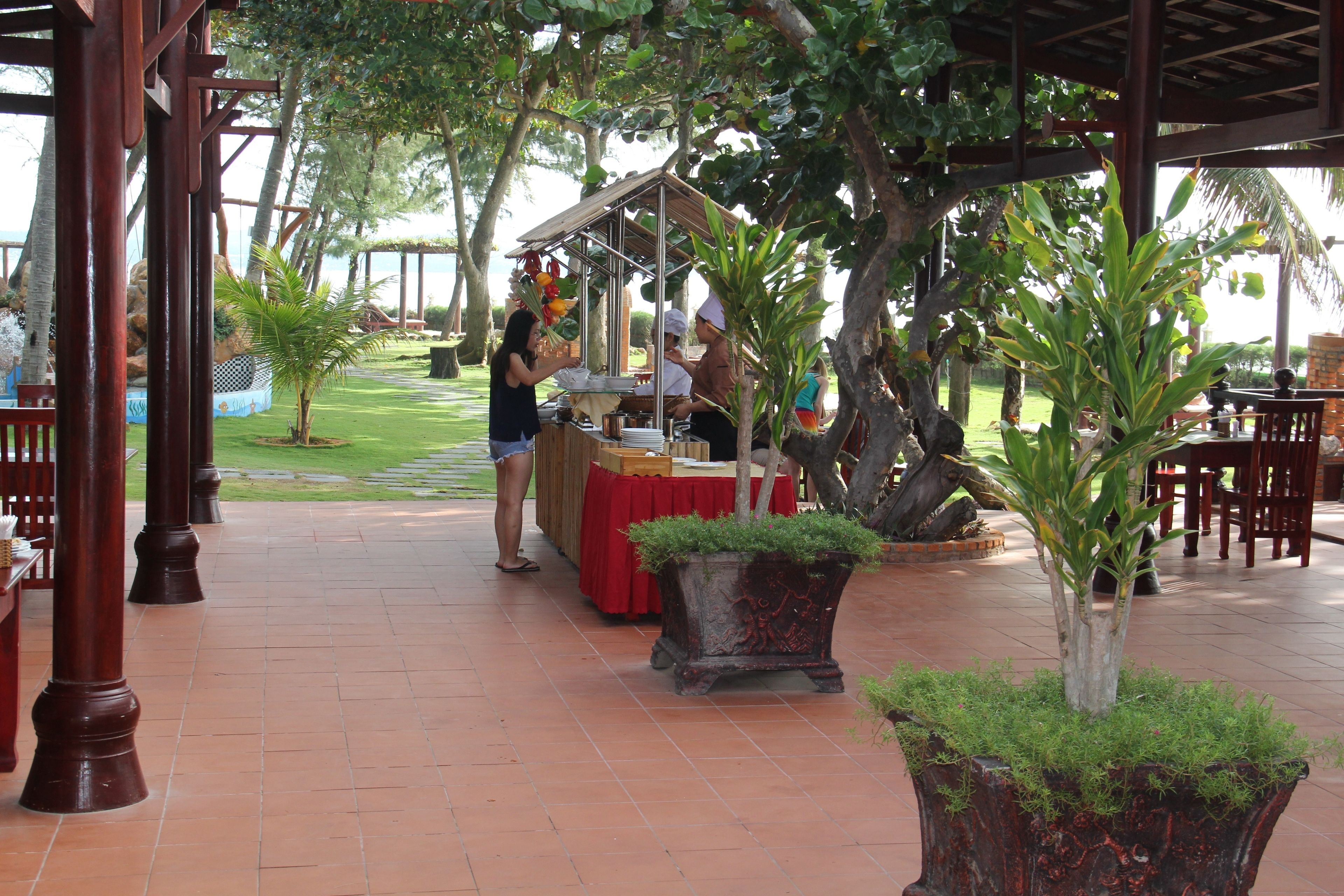 Zona pranzo all'aperto con area salotto coperta, uno stand gastronomico e piante in vaso.