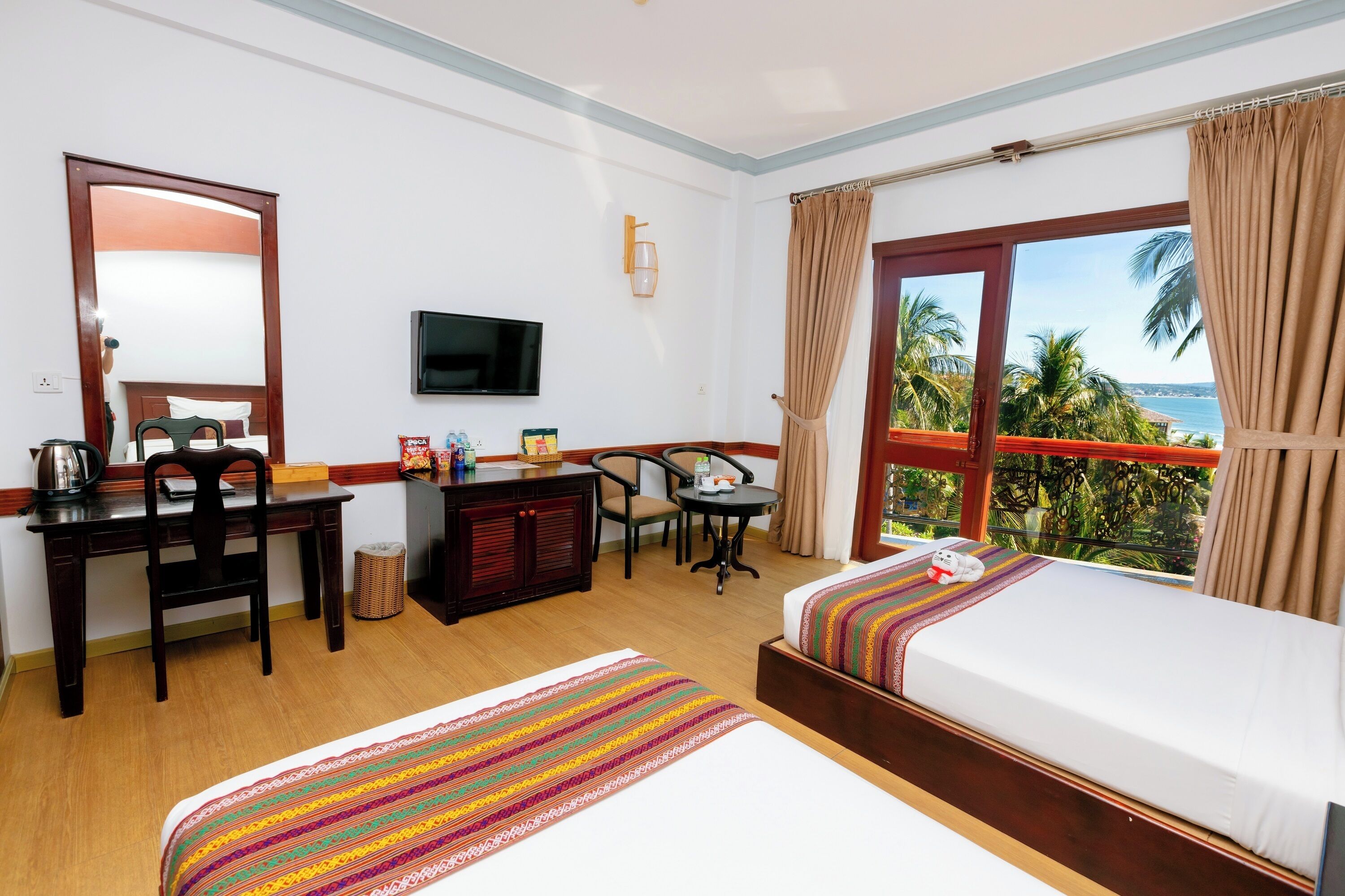 Quarto de hotel com cama, escrivaninha, cadeira, televisão e janela com vista para o oceano.