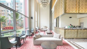 Eine großzügige Lobby mit einem roten Teppich mit Muster, einer Couch, Sesseln, einem runden Tisch und einem Empfangsbereich.