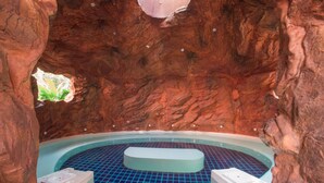 Ein Whirlpool mit blau gefliestem Boden, vor einer Felswand mit einem kleinen Fenster.