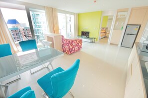 Una sala moderna con una mesa de vidrio, sillas azules, un sofá floral y un televisor.