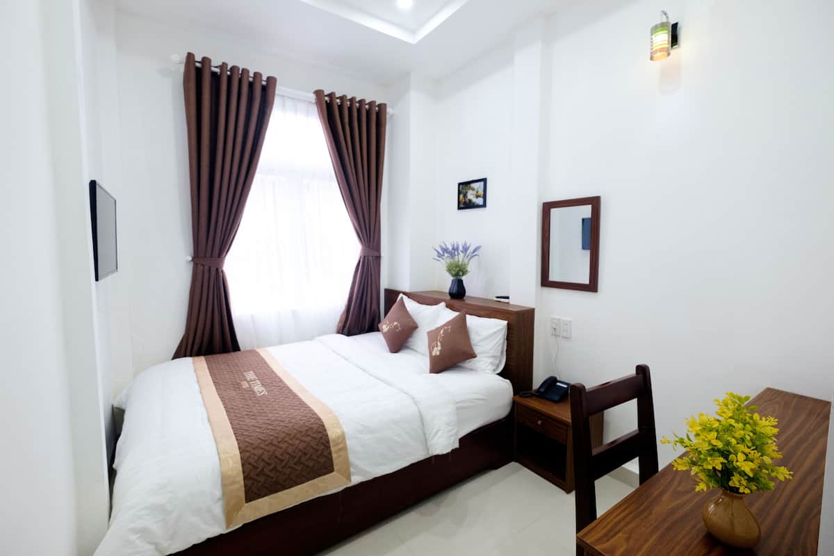 Habitación de hotel con cama, escritorio, silla, un jarrón con flores y un cuadro en la pared.