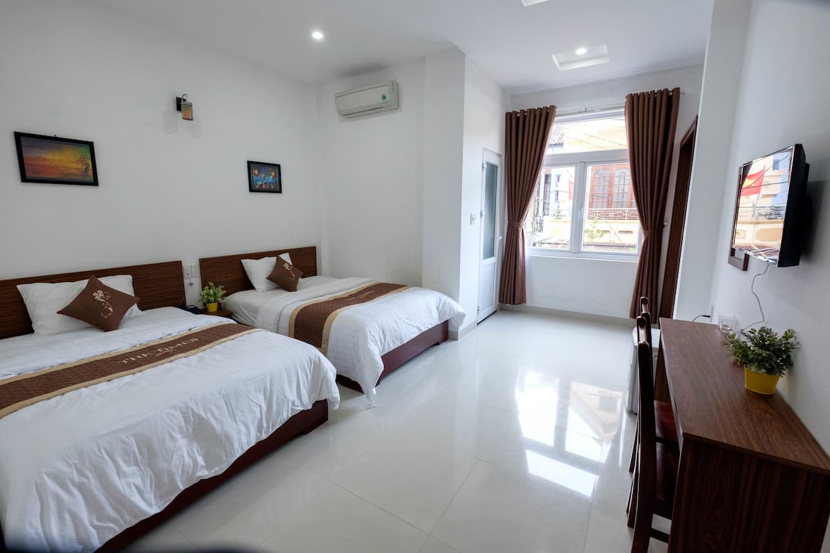 Habitación de hotel con dos camas, televisor, escritorio y ventana con cortinas.