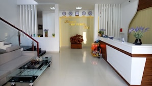 A modern hotel lobby with a reception desk, a sofa, a glass coffee table, and a staircase. - The Times Hotel (Hue)