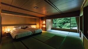 Une chambre de style japonais traditionnel, avec des tatamis, un lit double et une vue sur la verdure grâce à une grande fenêtre.
