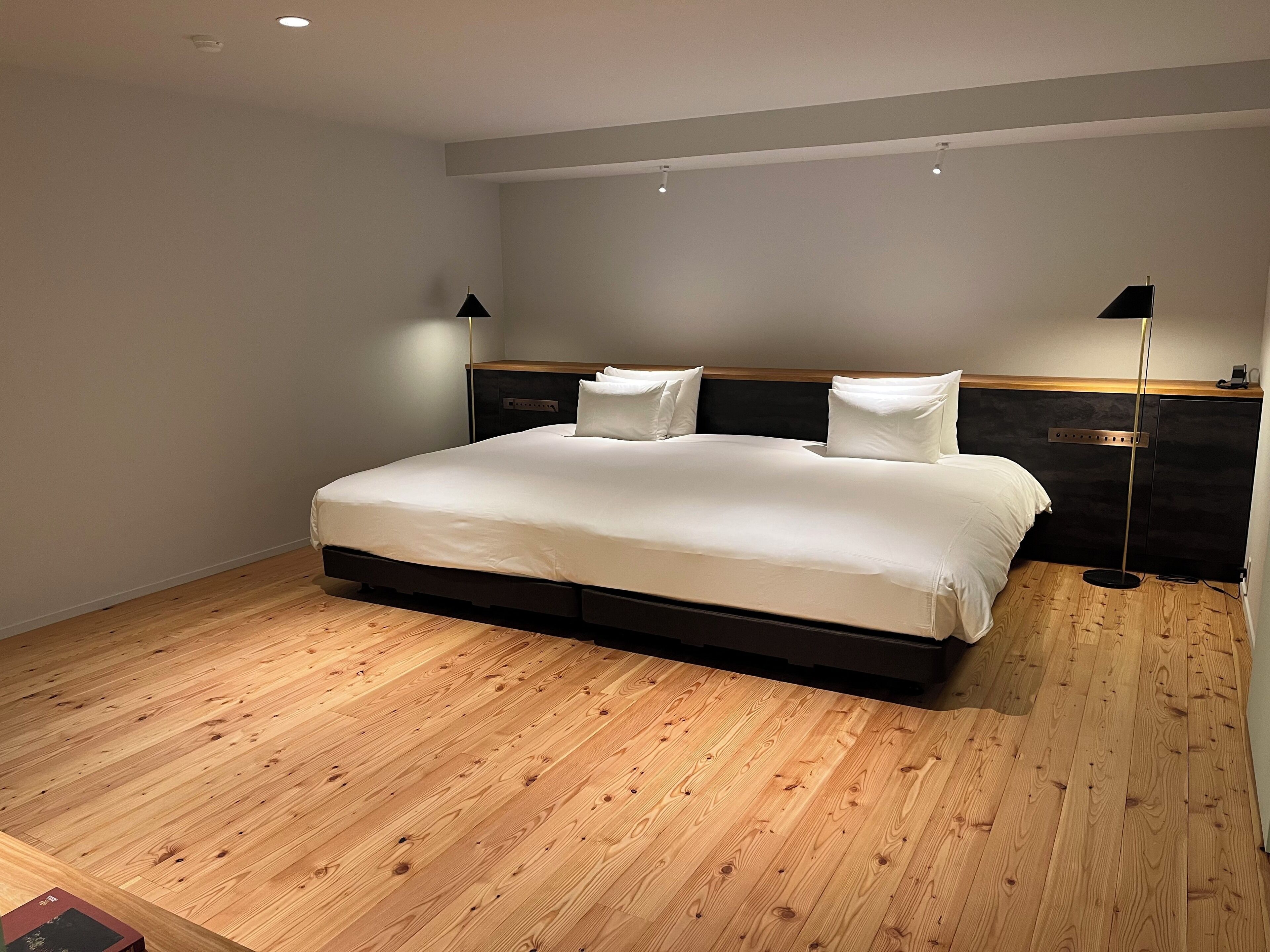 A modern hotel room with a large bed, wooden flooring, and two bedside lamps.
