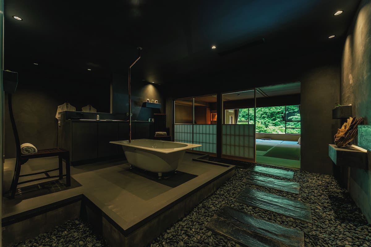 Un baño moderno con una bañera independiente, un banco de madera y un ventanal con vistas a zonas verdes.