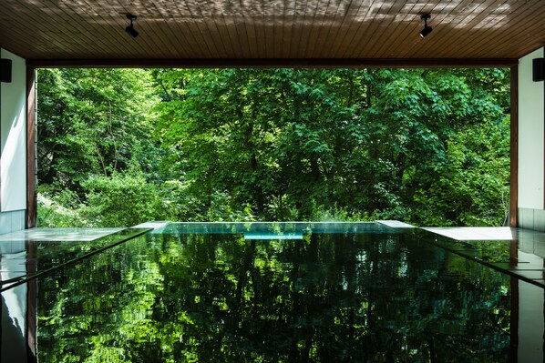 A modern indoor pool with a glass floor, surrounded by lush greenery.