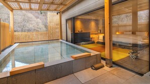 Une piscine intérieure moderne dotée d’une terrasse en bois, d’un espace sauna et d’un mur de verre offrant une vue sur l’extérieur.