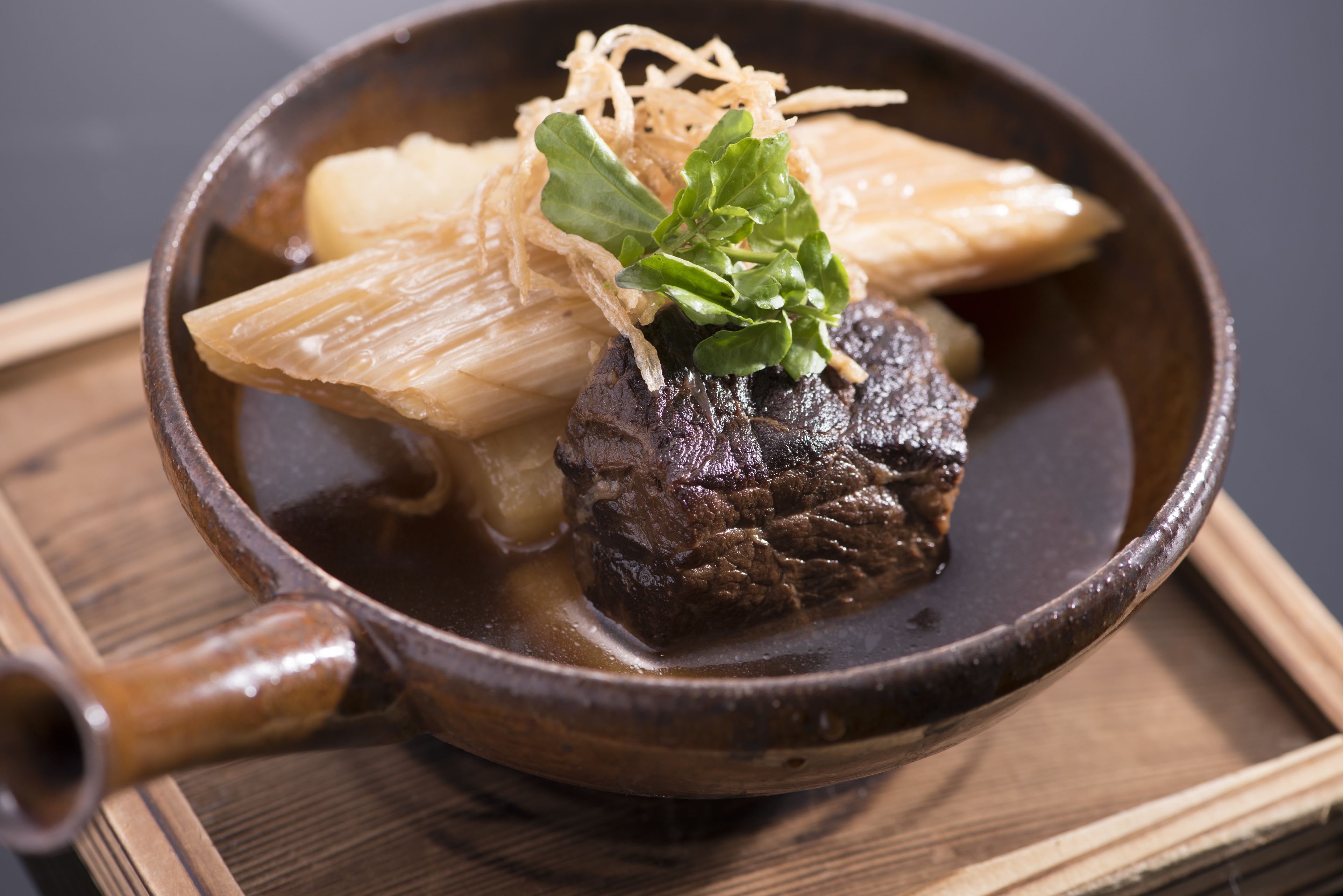 A bowl of beef with vegetables and noodles in a dark bowl.