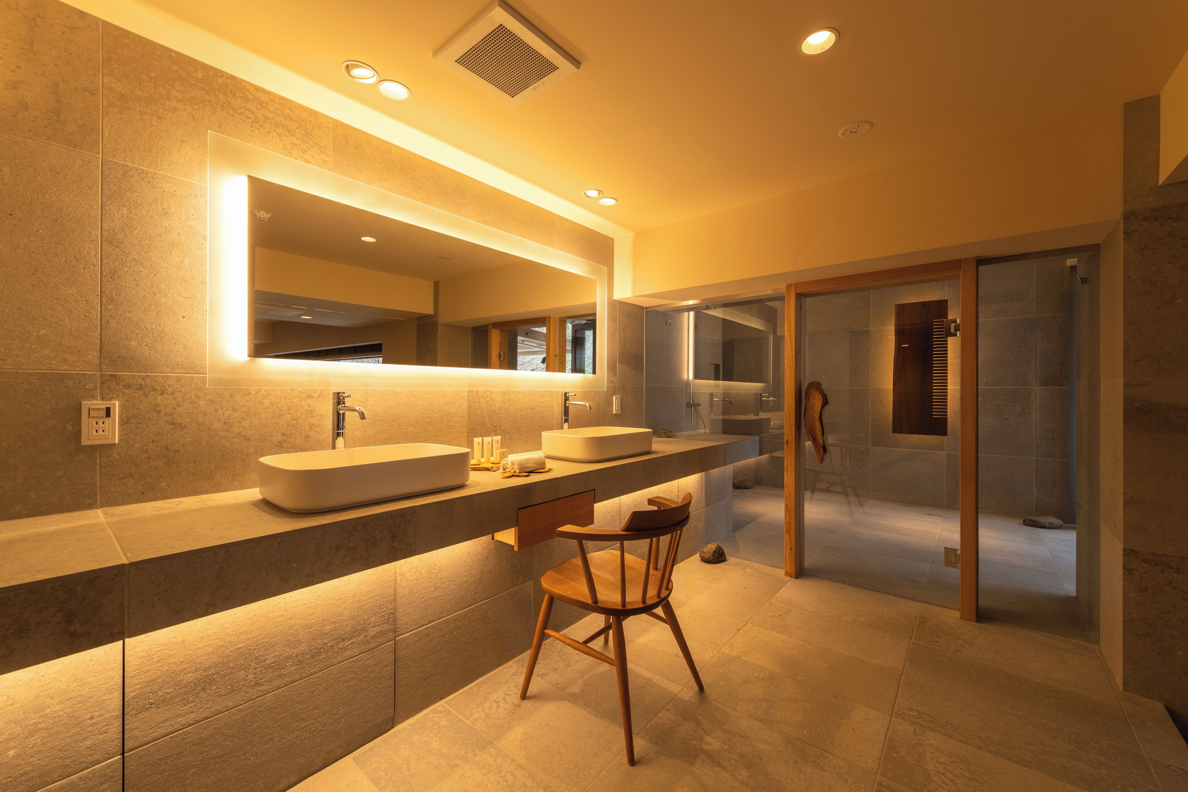 A modern bathroom with a large mirror, two sinks, and a shower area.