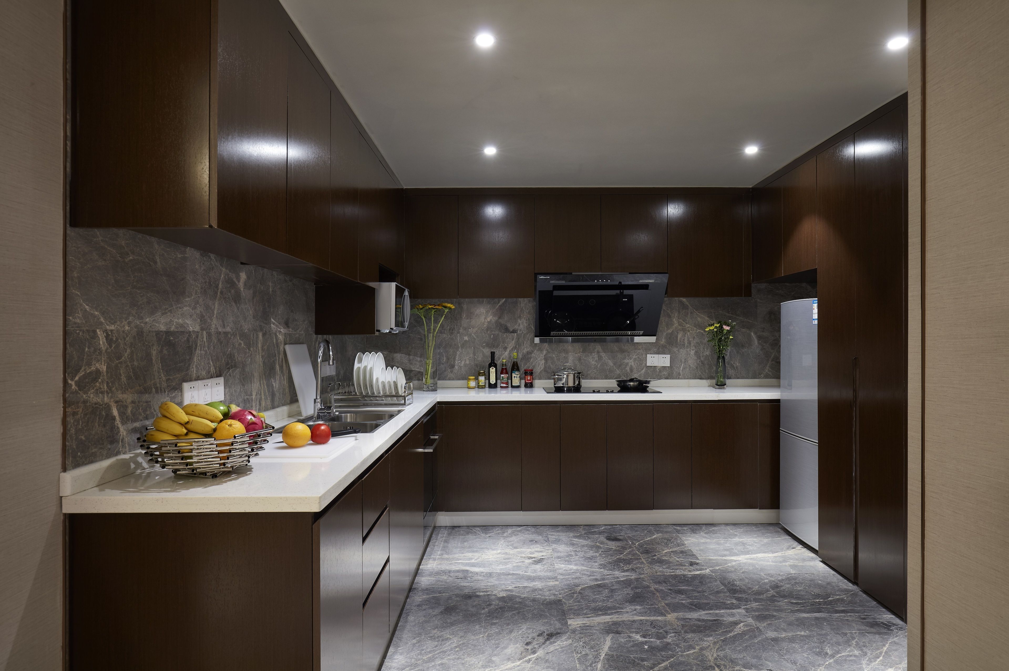 A modern kitchen with dark wood cabinets, a marble countertop, and a built-in oven.