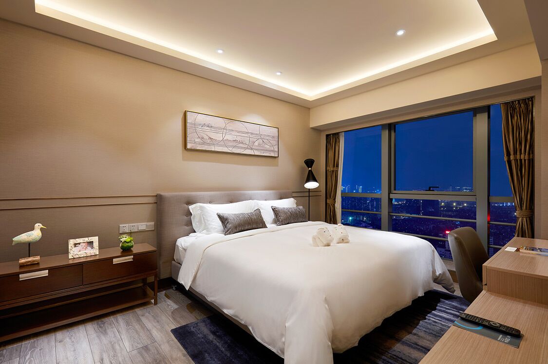 Quarto de hotel moderno com uma cama grande, uma escrivaninha e vista para a cidade à noite.