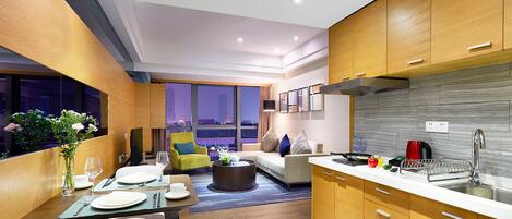 A modern kitchen and dining area with wooden cabinets, a dining table set for four, and a sofa in the living area.