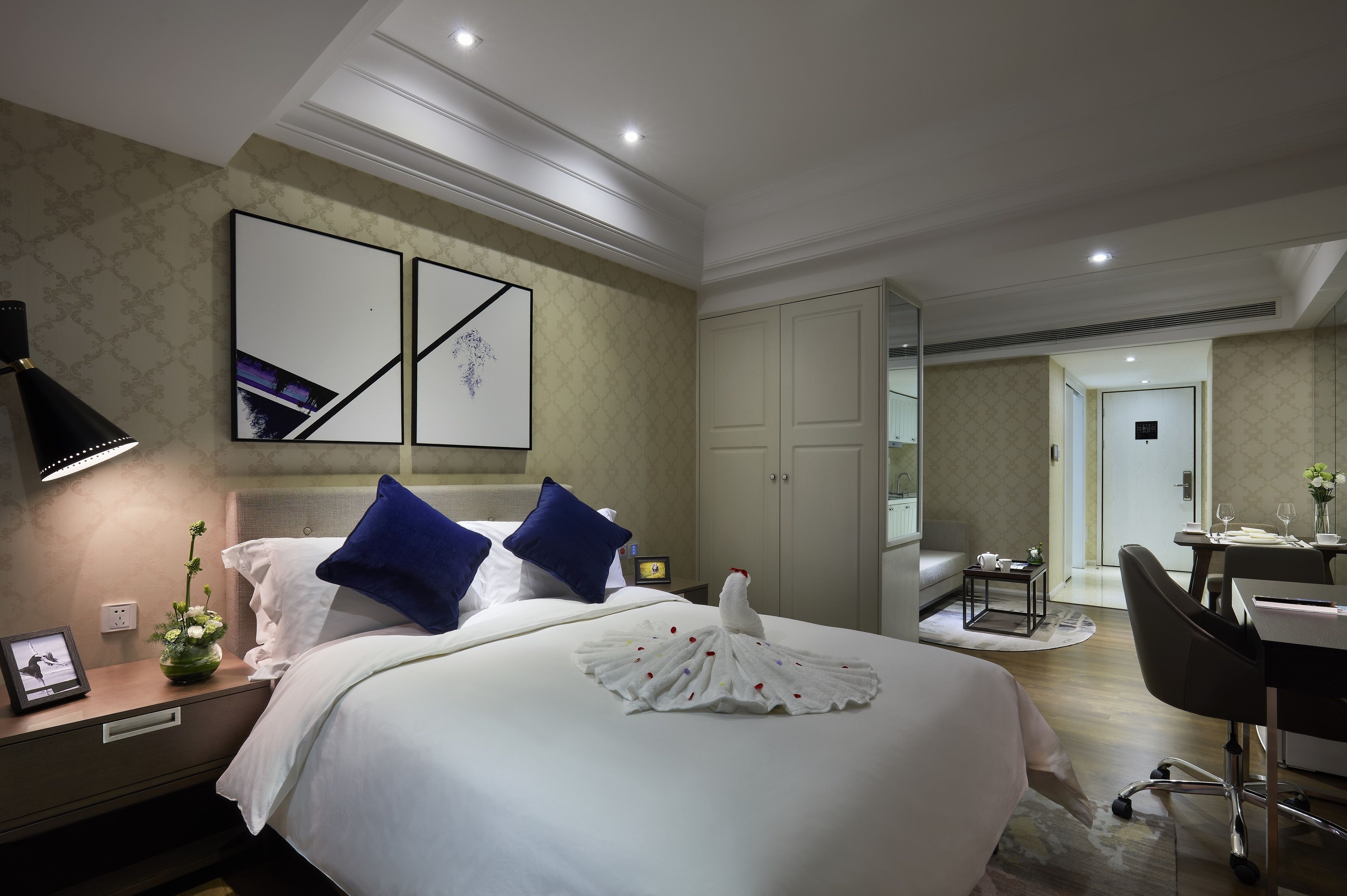 A hotel room with a large bed, a desk, a chair, and a dining area.