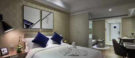 A hotel room with a large bed, a desk, a chair, and a dining area.
