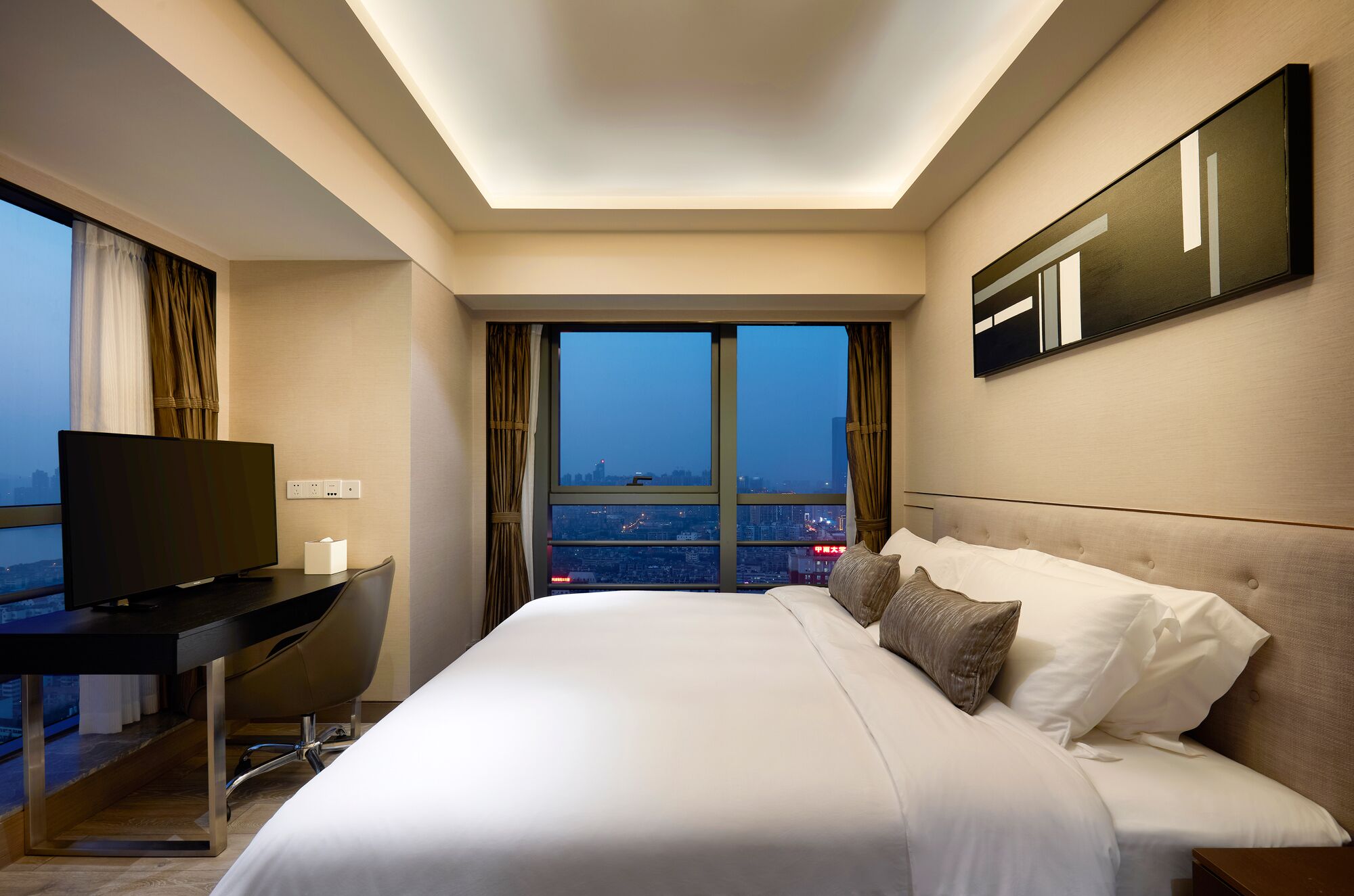 Ein Hotelzimmer mit einem Bett, einem Schreibtisch mit Fernseher und einem großen Fenster mit Blick auf die Stadt.