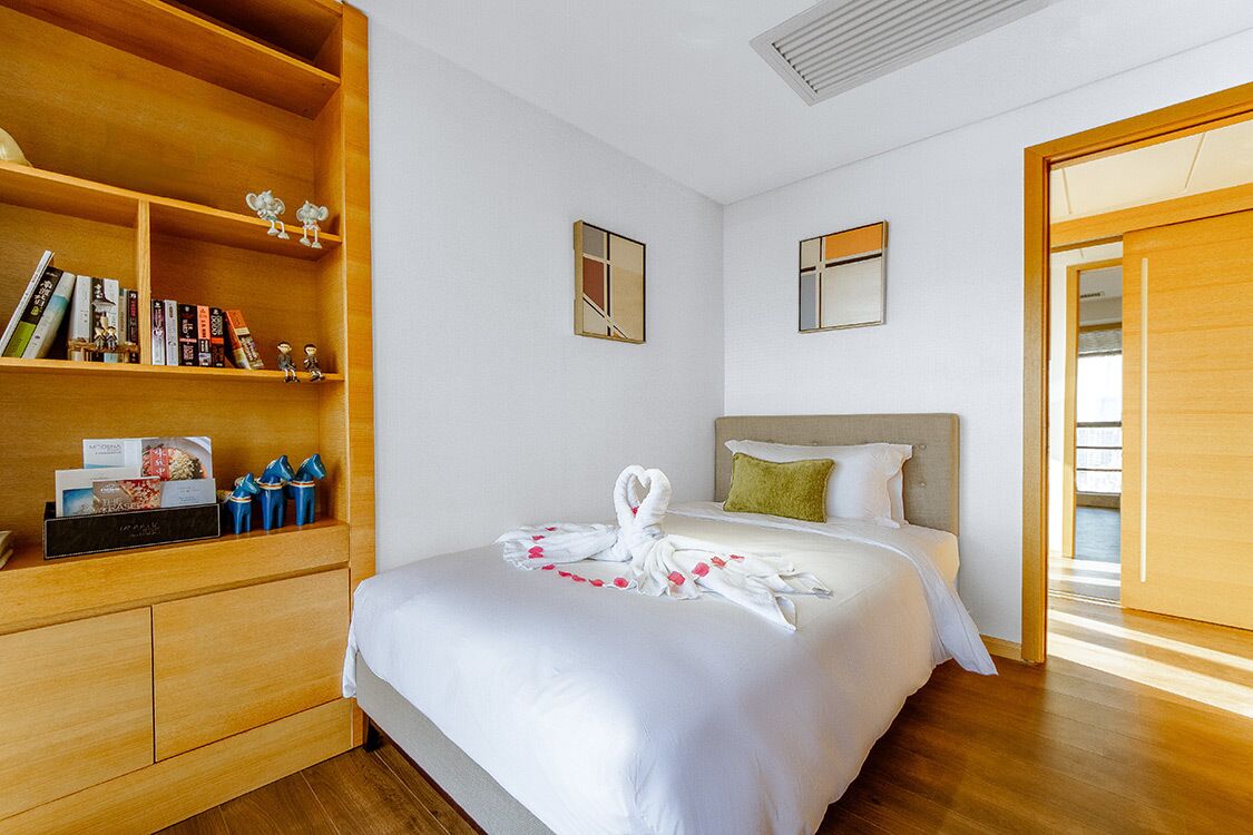Une chambre d’hôtel avec un grand lit, une armoire en bois et une petite étagère contenant des livres et des objets décoratifs.
