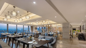 Un comedor moderno con varias mesas y sillas, ventanas amplias que ofrecen vista a la ciudad y luminarias decorativas.