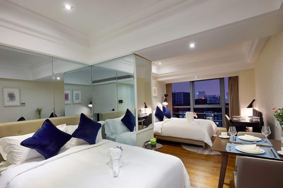 Ein Hotelzimmer mit zwei Betten, einem Essbereich und einem großen Fenster mit Blick auf die Stadt.